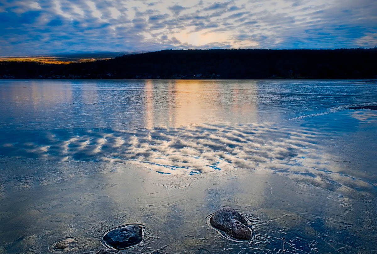I caught this photo at the start of sunset with the orange glow reflecting off the ice and the wavy clouds reflecting off some open water at Otisco Lake.