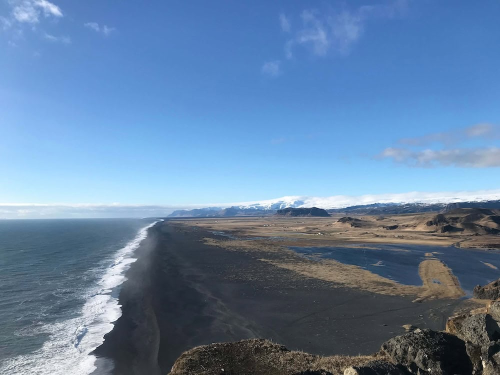 Ocean meeting black sand beach with mountains and a glacier in the distance on Iceland's South Coast