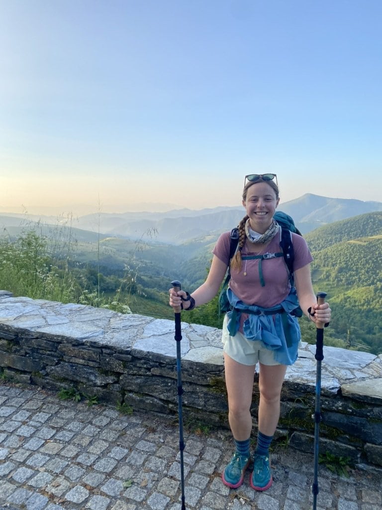 Female hiker holding hiking poles and smiling in front of a deep valley and mountains
