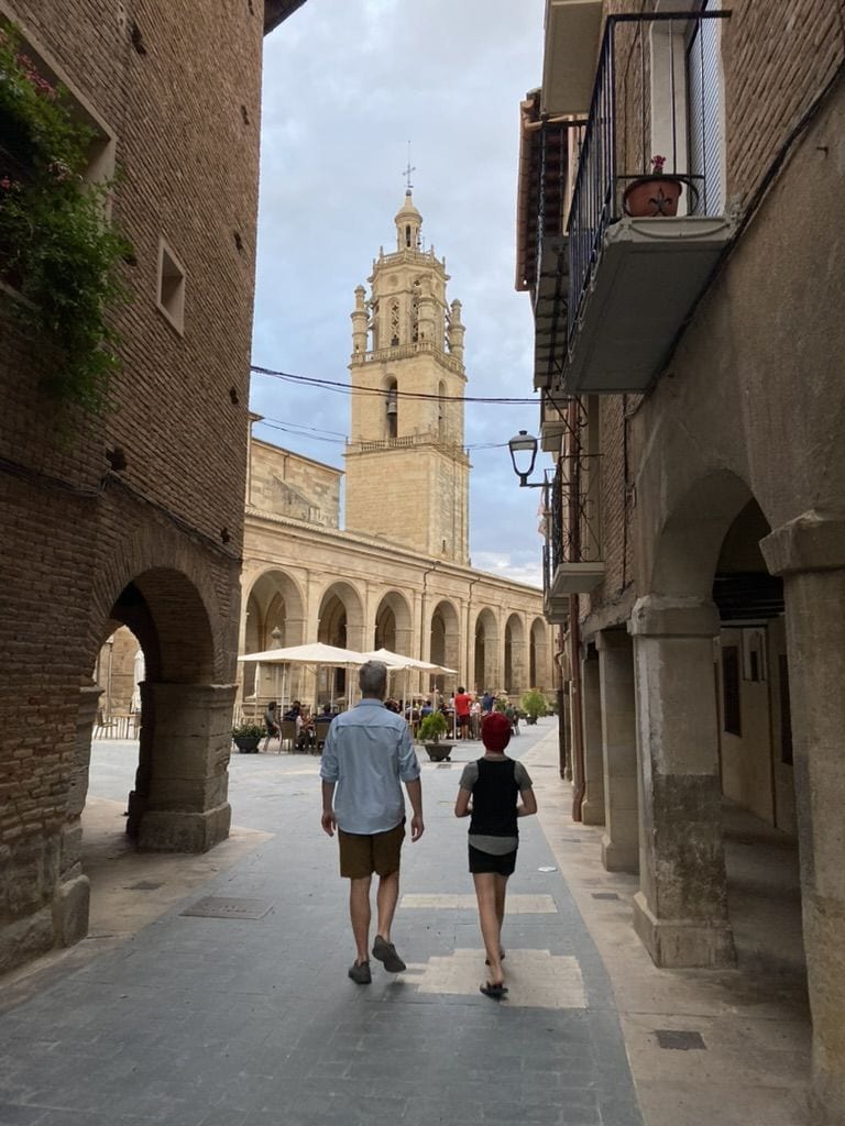 Two people walking down an old city street in front of a cathedral in Los Arcos, Spain