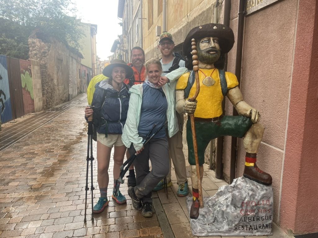 Four people smiling with a statue of a pilgrim outside of an albergue on the Camino in Belorado Spain