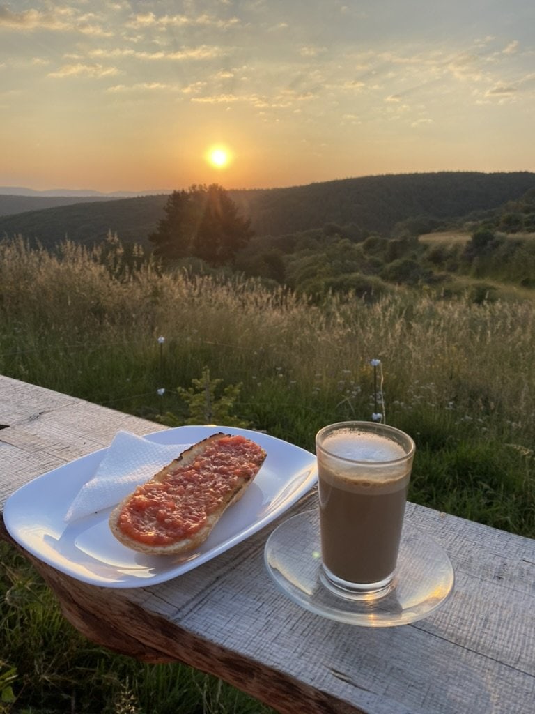 A view of the sunrise over the mountains with toast and coffee outside along the Camino Francés