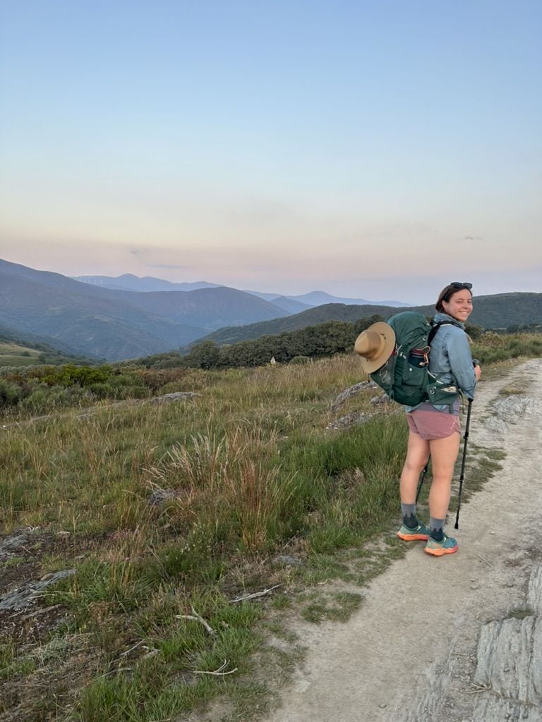Woman hiking through the mountains at sunrise, looking back and smiling at the camera along the Camino Francés