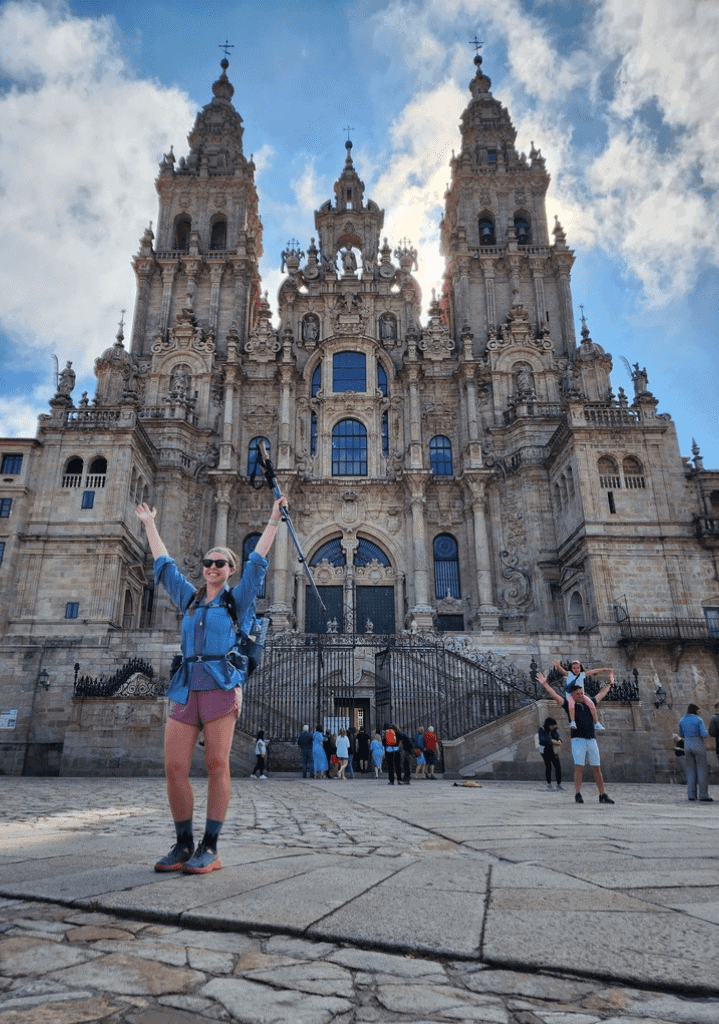 Hiker with arms in the air in front of a cathedral in Santiago de Compostela, Spain at the end of the Camino Francés