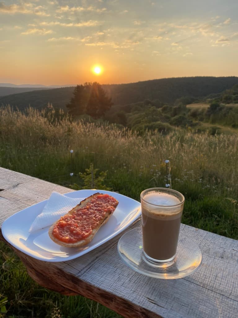 Toast and coffee on a deck ledge outside with a view of the sun rising over the mountains along the Camino de Santiago