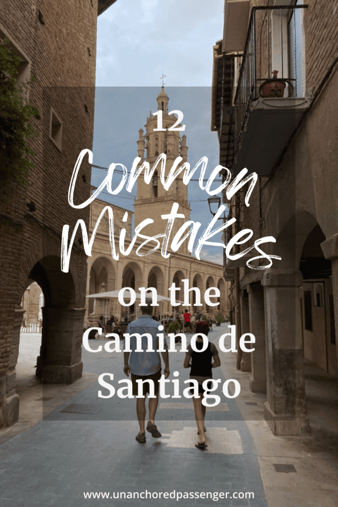 Two people walking down an old city street in front of a cathedral in Los Arcos, Spain with text that reads, "12 Common Mistakes on the Camino de Santiago"