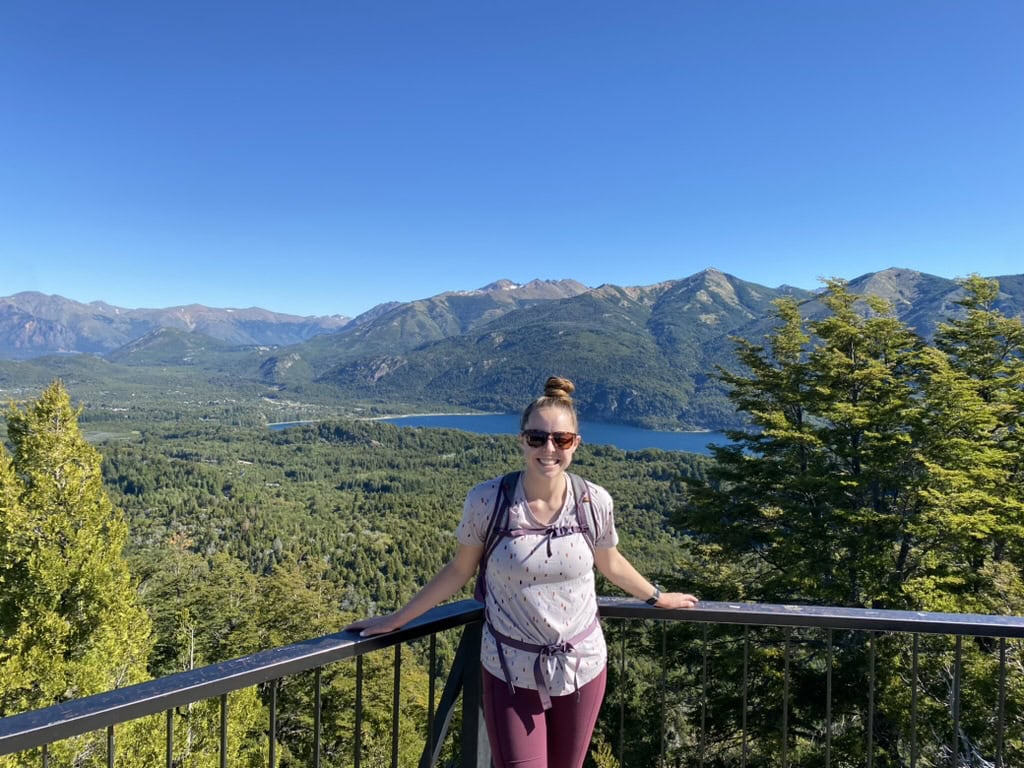 Woman smiling at an overlook of a bright blue lake surrounded by mountains in Bariloche, Argentina