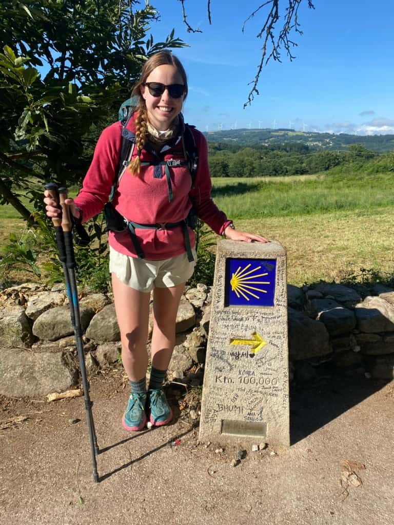 Woman with hiking poles smiling at a Camino de Santiago trail marker