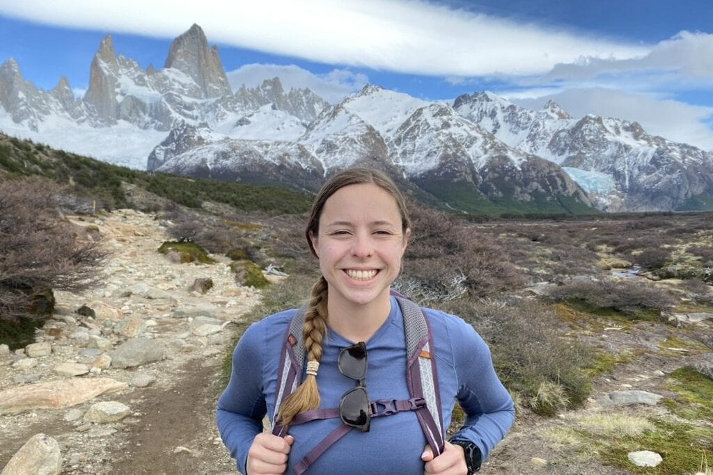 Woman smiling on a hiking trail with mountains in the background