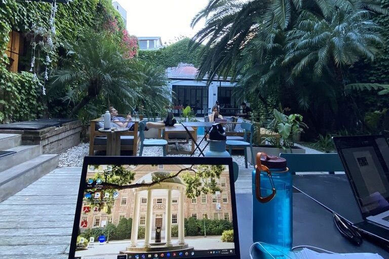 Laptop in a coworking space with palm trees and other green plants and people working in the background