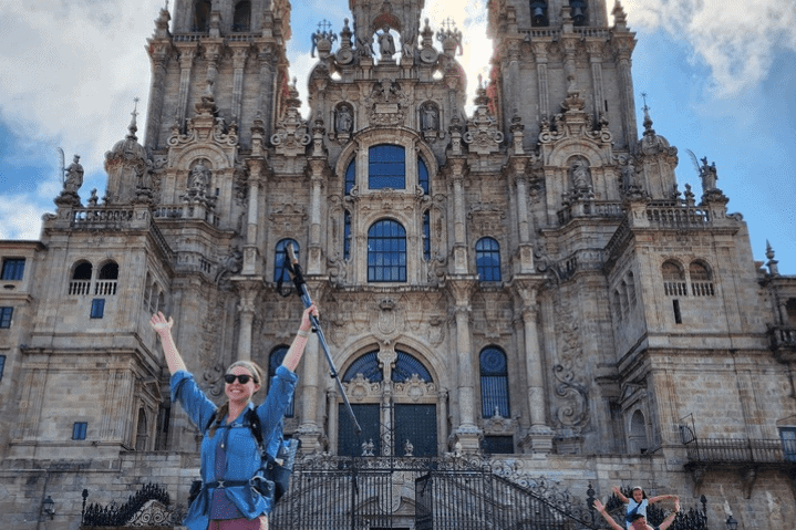 Hiker with arms in the air in front of a cathedral in Santiago de Compostela, Spain