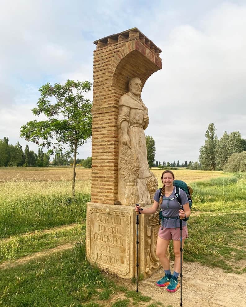 Female hiker smiling in front of a statue at the halfway point of the Camino Francés