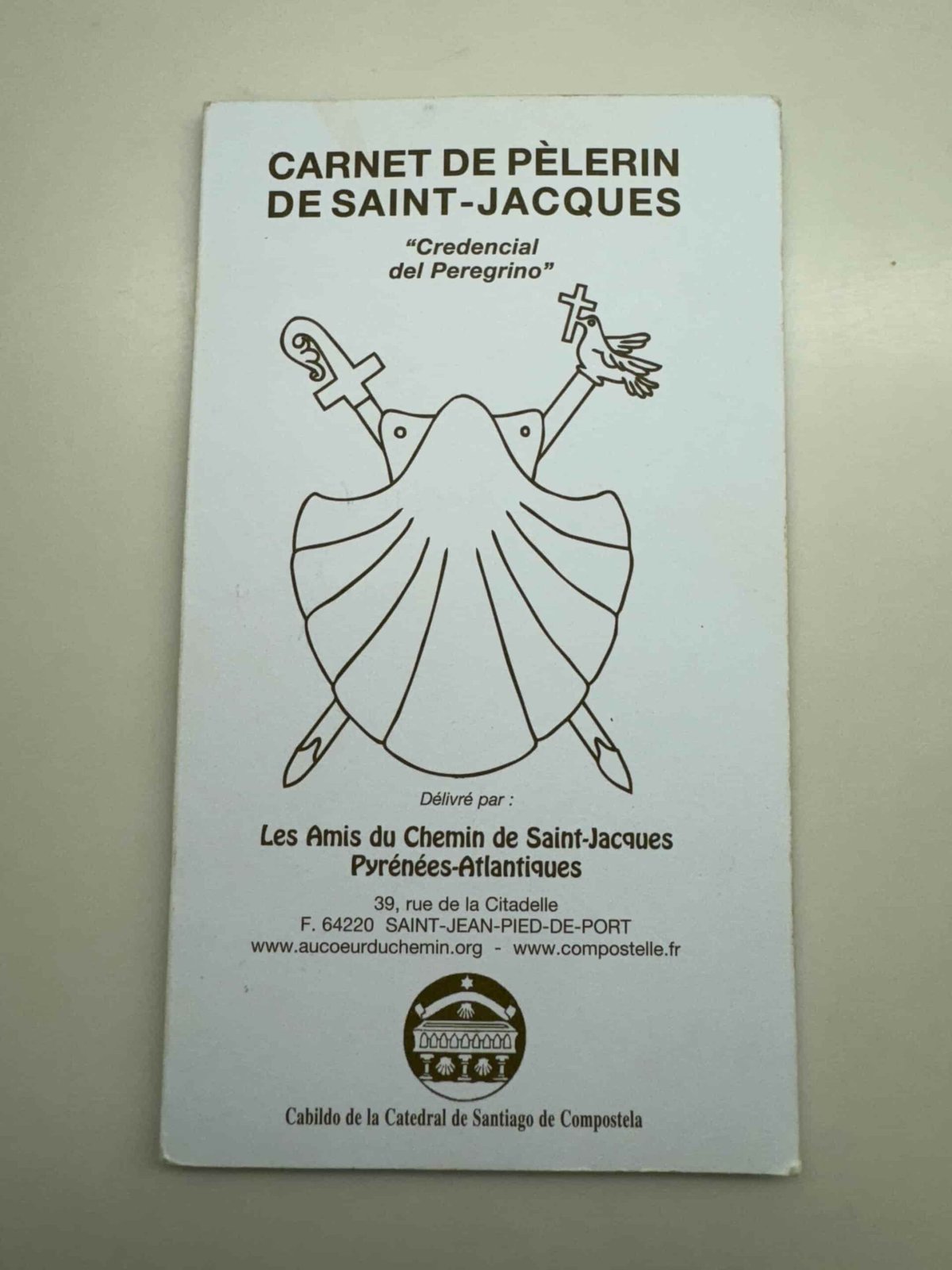 Front of the Camino de Santiago passport book with an image of a shell, two swords, and a dove with a cross