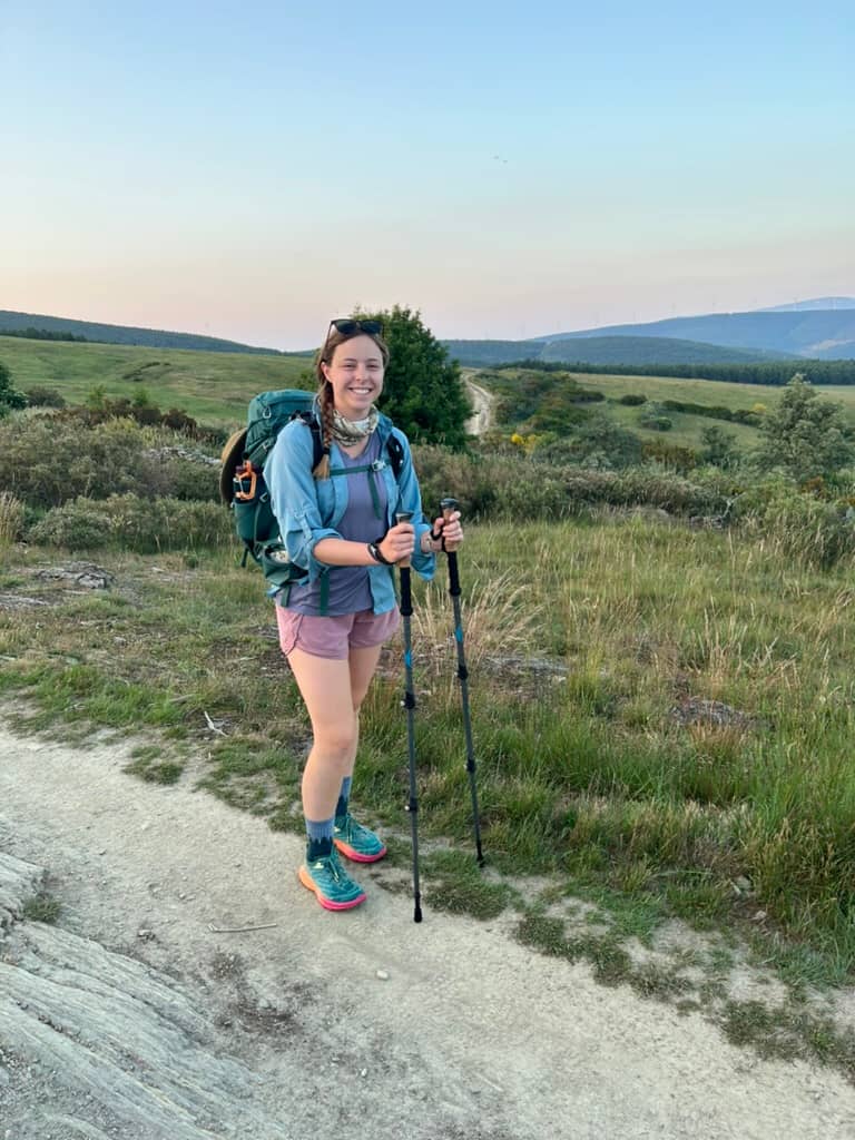 Hiker with a pack and trekking poles smiling in the early morning in the mountains