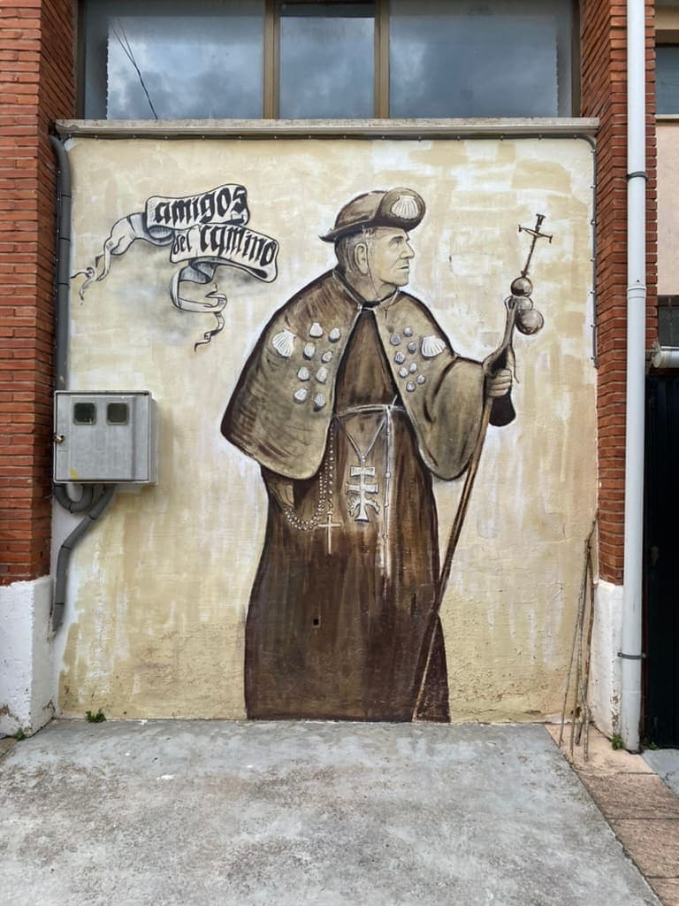 Mural of a historic Camino de Santiago pilgrim on the side of an albergue along the Camino Francés.