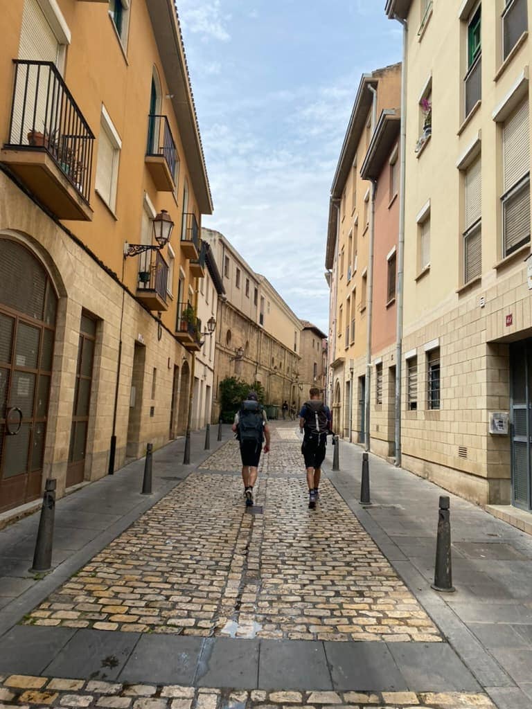 Two pilgrims walking through an empty cobblestone street in Logroño, Spain along the Camino Francés.