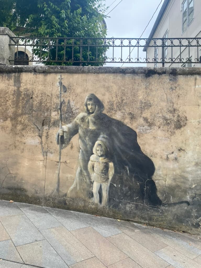 Mural on a wall in Sarria, Spain of a historic pilgrim and child wearing a traditional cloak and holding a staff with a gourd
