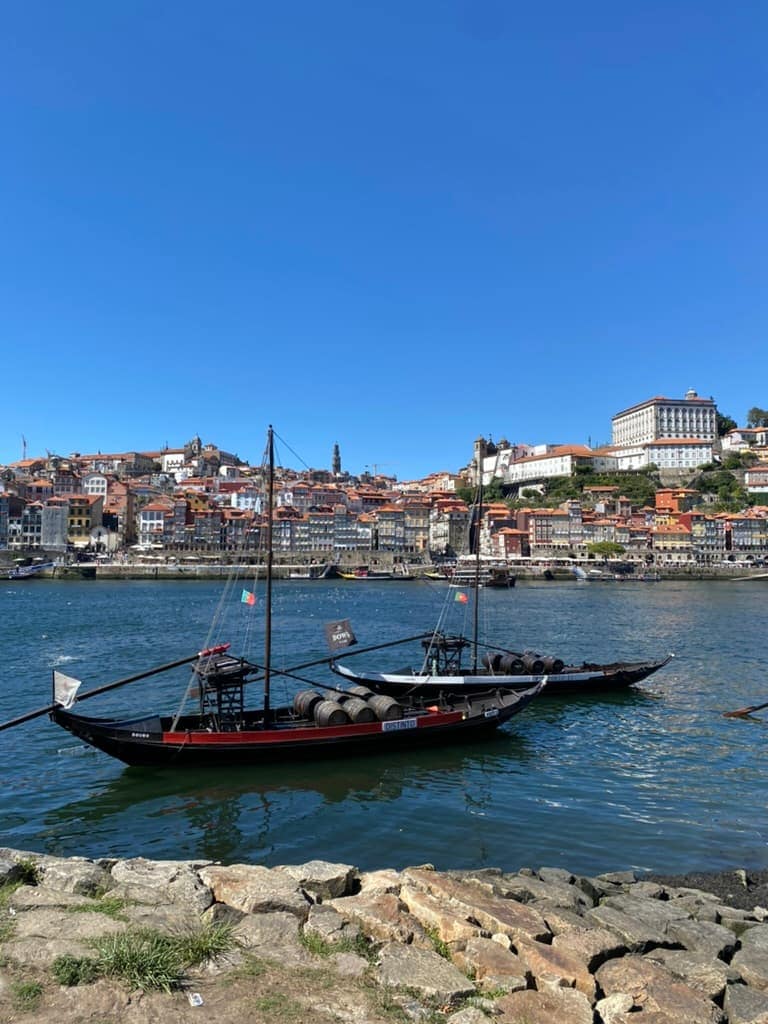 Two boats anchored on the Douro River in Porto, Portugal with the old town in the background.