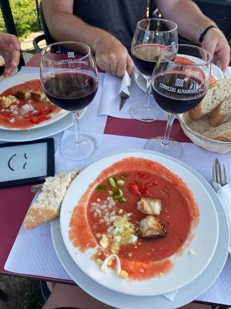 Bowl of gazpacho with red wine glasses and bread around it as part of the first course of a pilgrim meal on the Camino Francés.