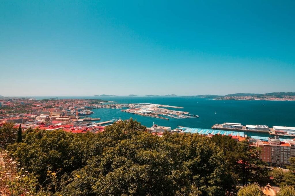 Looking out over Vigo, Spain from above with views of a city full of red roofed buildings below along a vibrant blue harbor