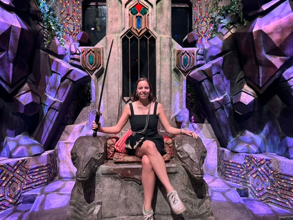 Mikala sitting on a Medieval-looking throne at Wētā Workshop Unleashed in Auckland New Zealand.