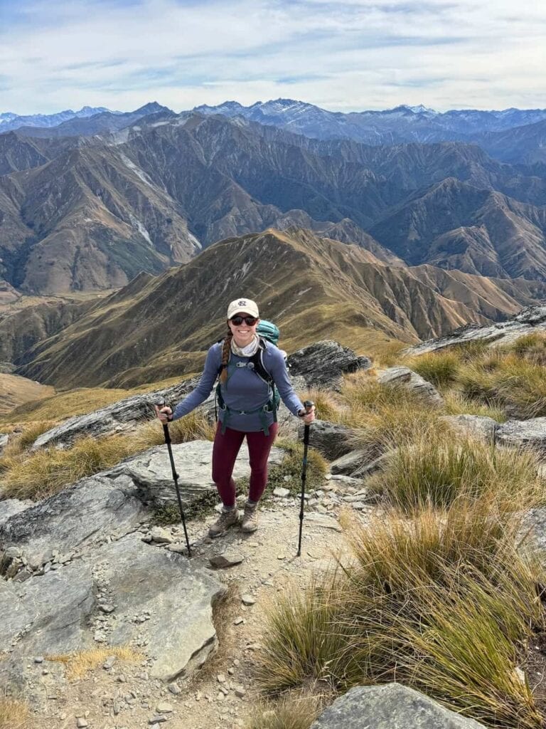 Mikala smiling with mountains in the background on Mount Lomond in New Zealand