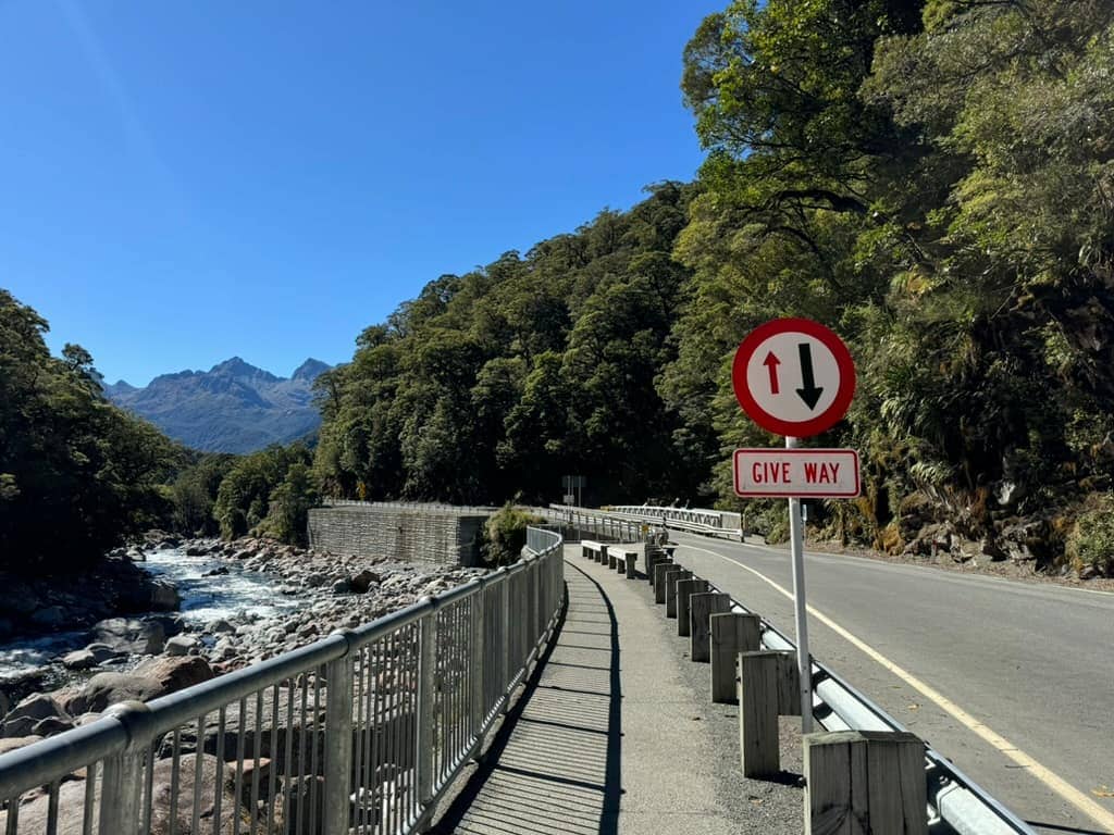 Sign with two arrows that says "Give Way" alongside a road in New Zealand before a one-lane bridge.