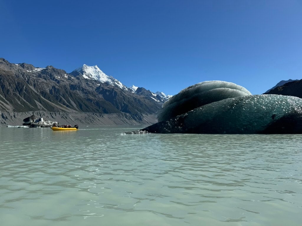 Glacial like with an iceberg, yellow boat, and Mount Cook in the distance.