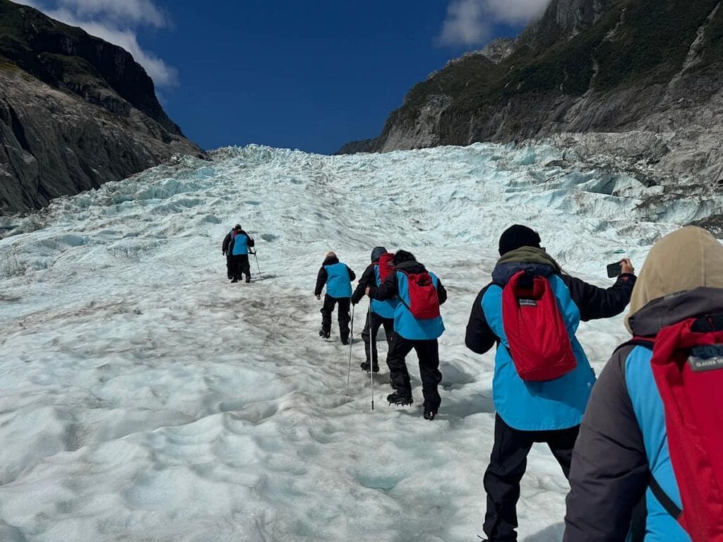 Hikers walking in a line on Fox Glacier behind a guide in New Zealand.