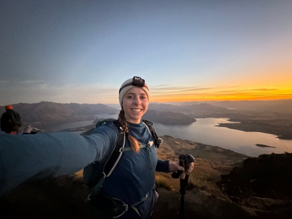 Mikala taking a selfie on the Roy's Peak summit at sunrise wearing her headlamp.