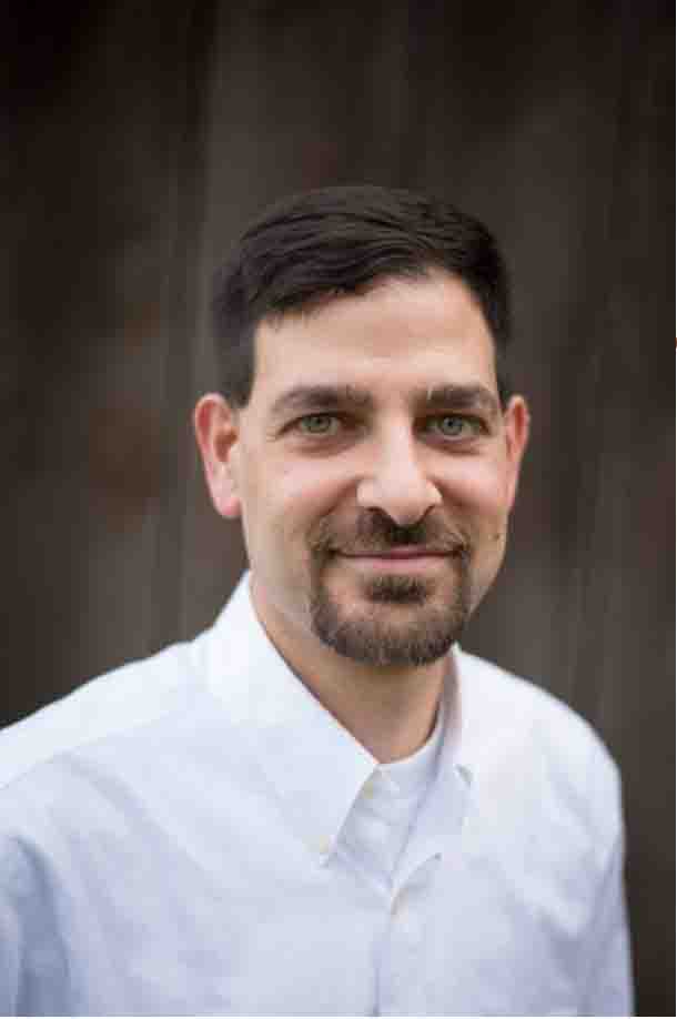 Man with short hair and goatee, wearing a white shirt, smiling slightly against a dark background. Solve your lice problems with Lice Nannies USA.