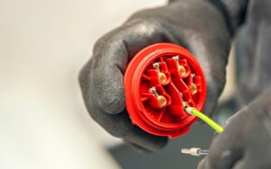 Close-up of gloved hands wiring a red industrial connector.