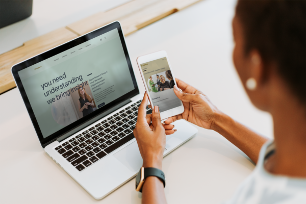 A woman is using her phone to look at the Sapere website on a laptop.