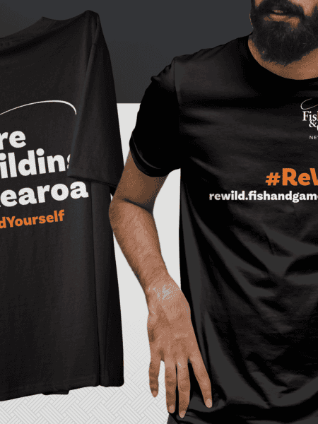 Two black T-shirts with environmental messages: left shirt reads "We're rewilding Aotearoa #ReWildYourself," right shirt has "Fish & Game New Zealand" logo and "#ReWild" slogan with web address.