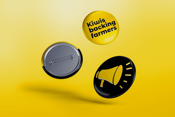 Three buttons drifting mid-air against a yellow background. One button shows the message "Kiwis backing farmers" in black text on a yellow background. Another button features a yellow megaphone graphic on a black background, while the third button displays its pin-back.