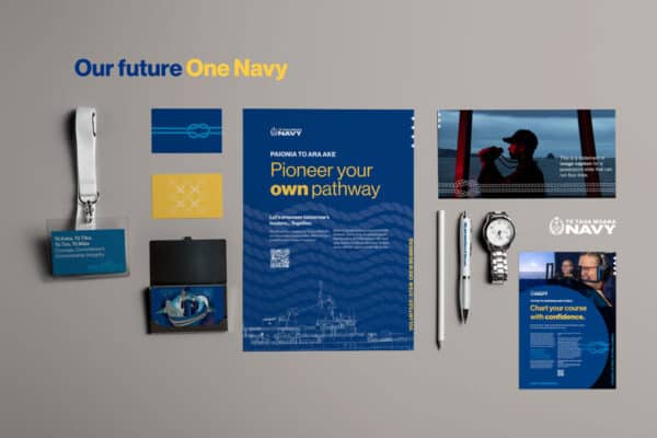 An arrangement of navy comms materials includes brochures, ID cards, a pen, a watch, and a lanyard. The central brochure emphasizes "Pioneer your own pathway" with navy imagery and logo. The overall theme promotes confidence and pathways in the Navy.