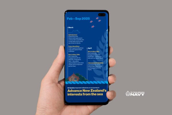 A hand holds a smartphone displaying a New Zealand Navy schedule for February to September 2025. It features events and missions listed for March and April against a blue background with navy-themed graphics.