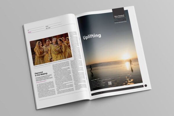 An open magazine displaying two pages. The left page features an article with an image of people in traditional attire. The right page is an advertisement with the text "Uplifting" over a serene beach sunset scene, showing silhouettes of people by the water.