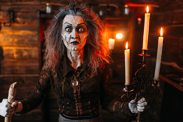 Scary witch with candlestick and cane reads spell מכשפה