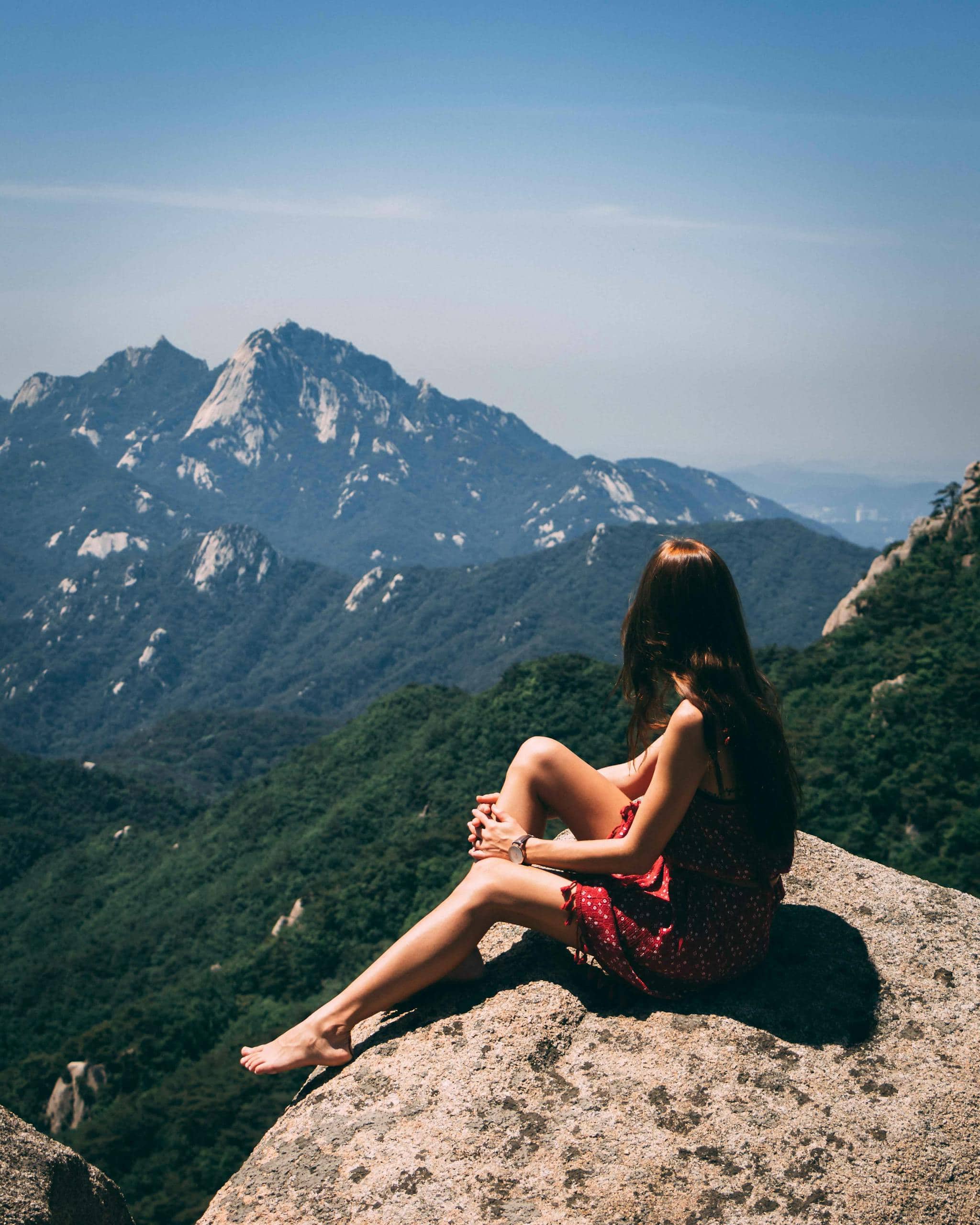 A woman sitting on a rock, admiring scenic mountain views during summer.