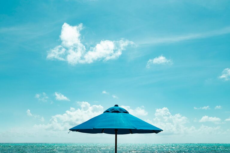 close up photo of blue parasol near body of water under blue sky