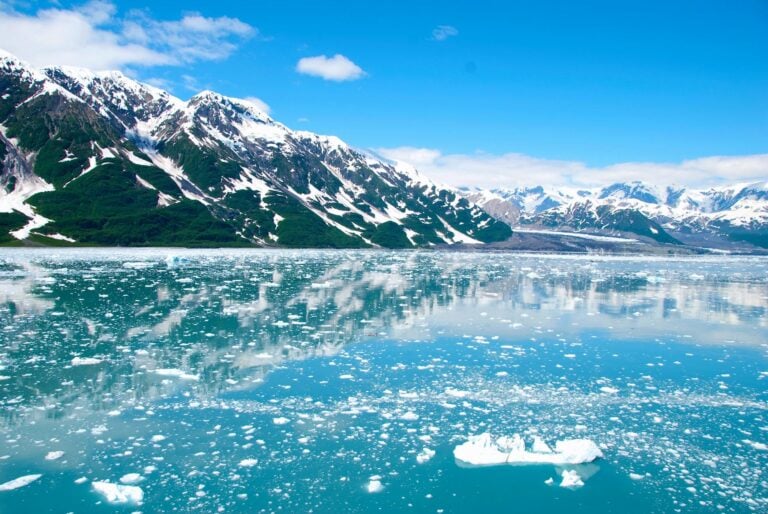 mountain filled with snow near calm sea under white clouds and blue sky during daytime