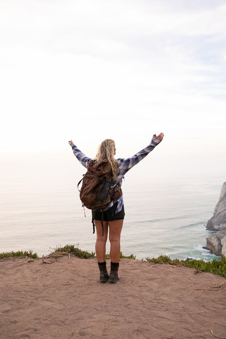 Woman Standing on Cliff with Arms Raised