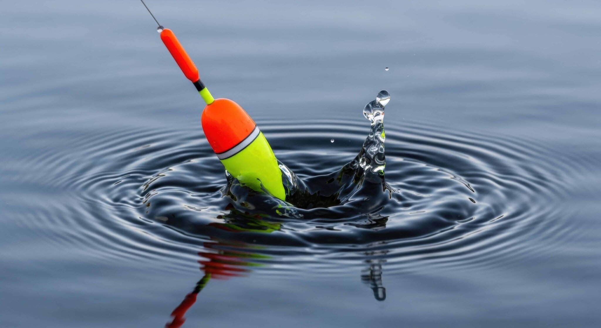 Bright fishing bobber splashing into calm water