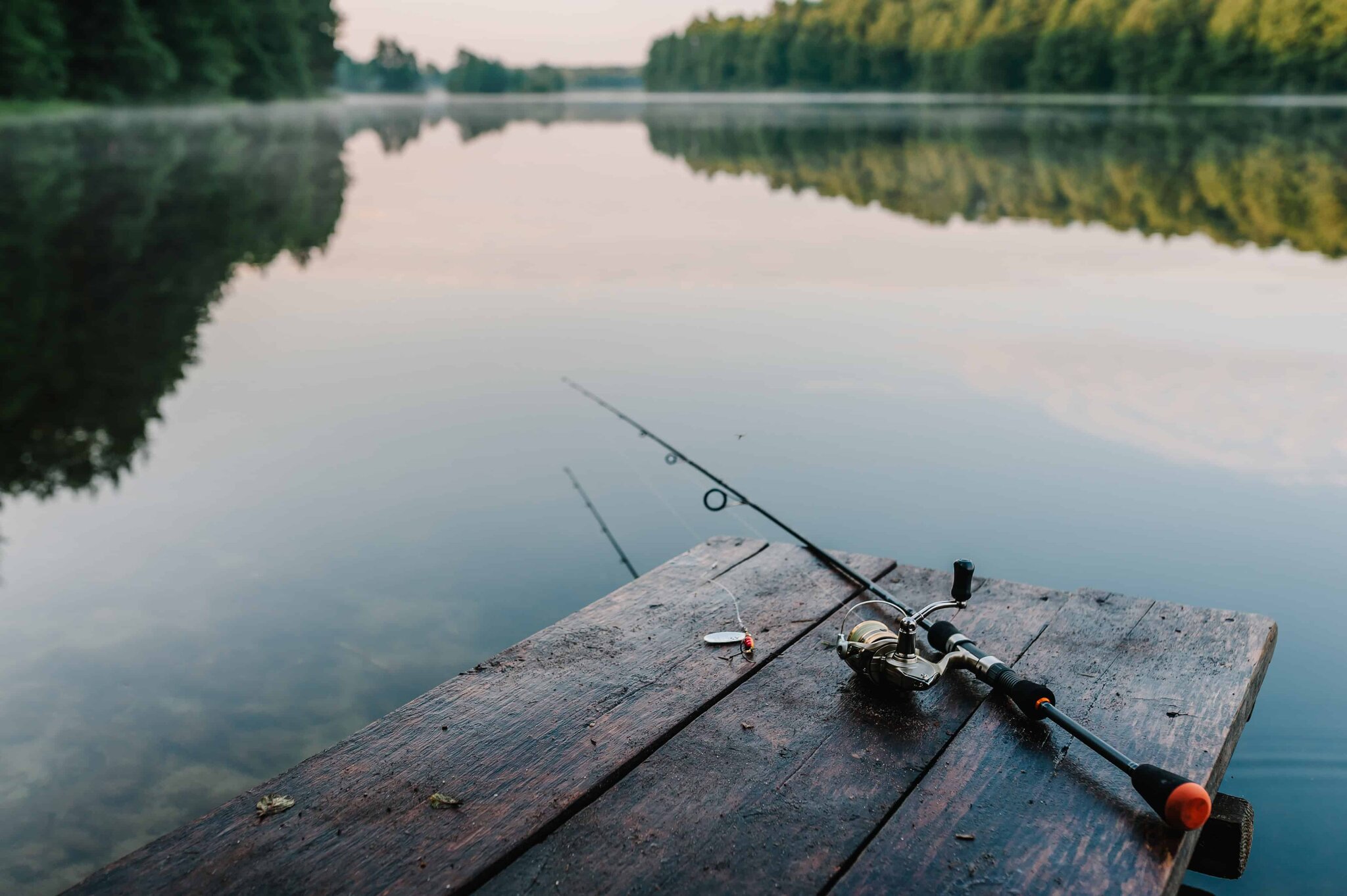 Fishing rod, spoon lure, and hooks on a brown wooden background