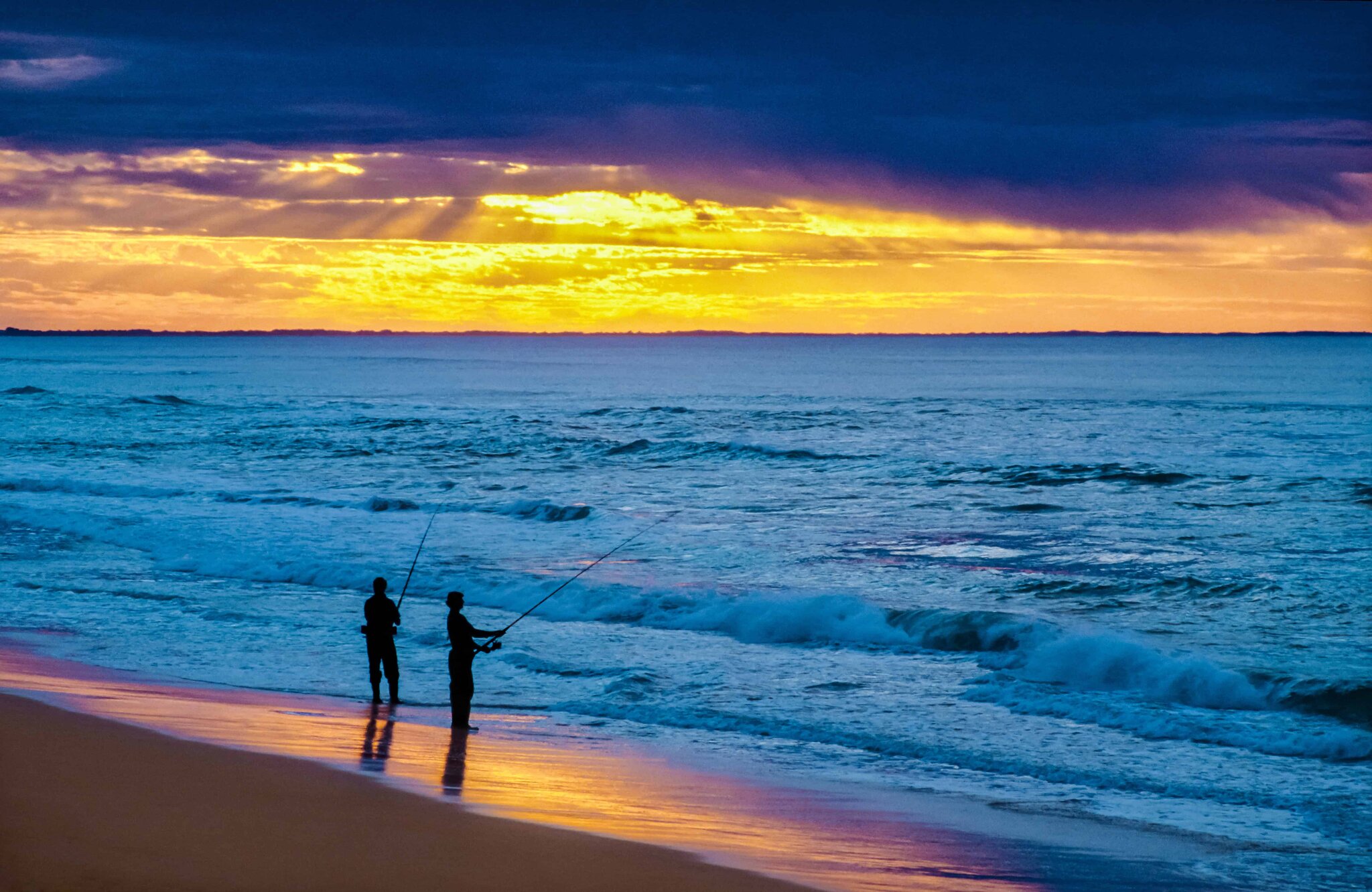 Beach angler silhouetted against incoming waves and dark storm clouds