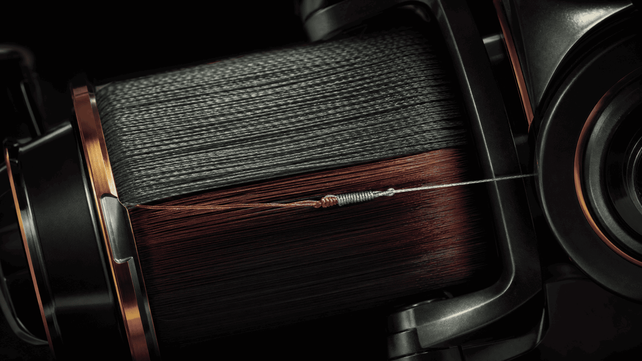 Spinning reel spool cutaway showing burgundy monofilament backing beneath braided line, connection knot lit dramatically