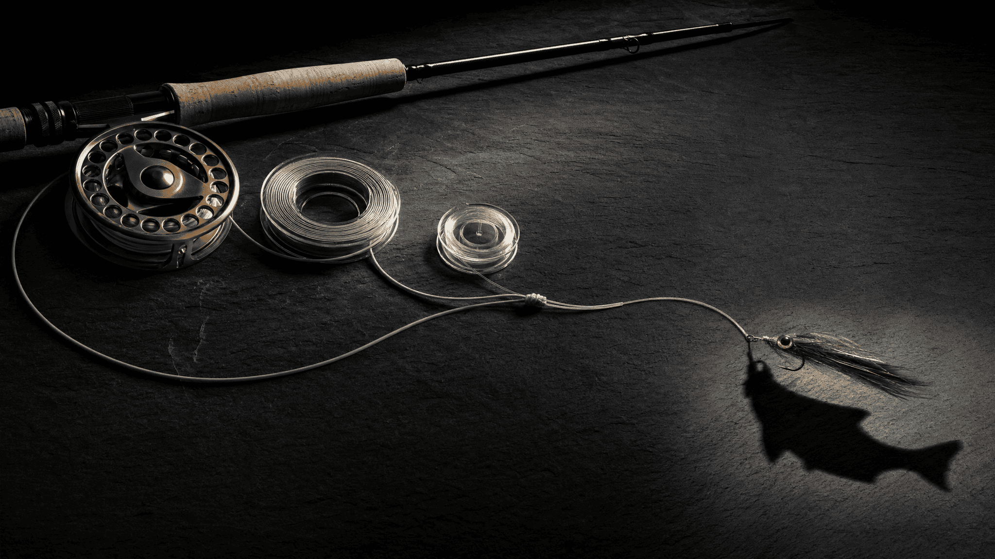Rod, reel, line, leader, knot, and lure arranged as a deliberate chain on dark slate under dramatic light