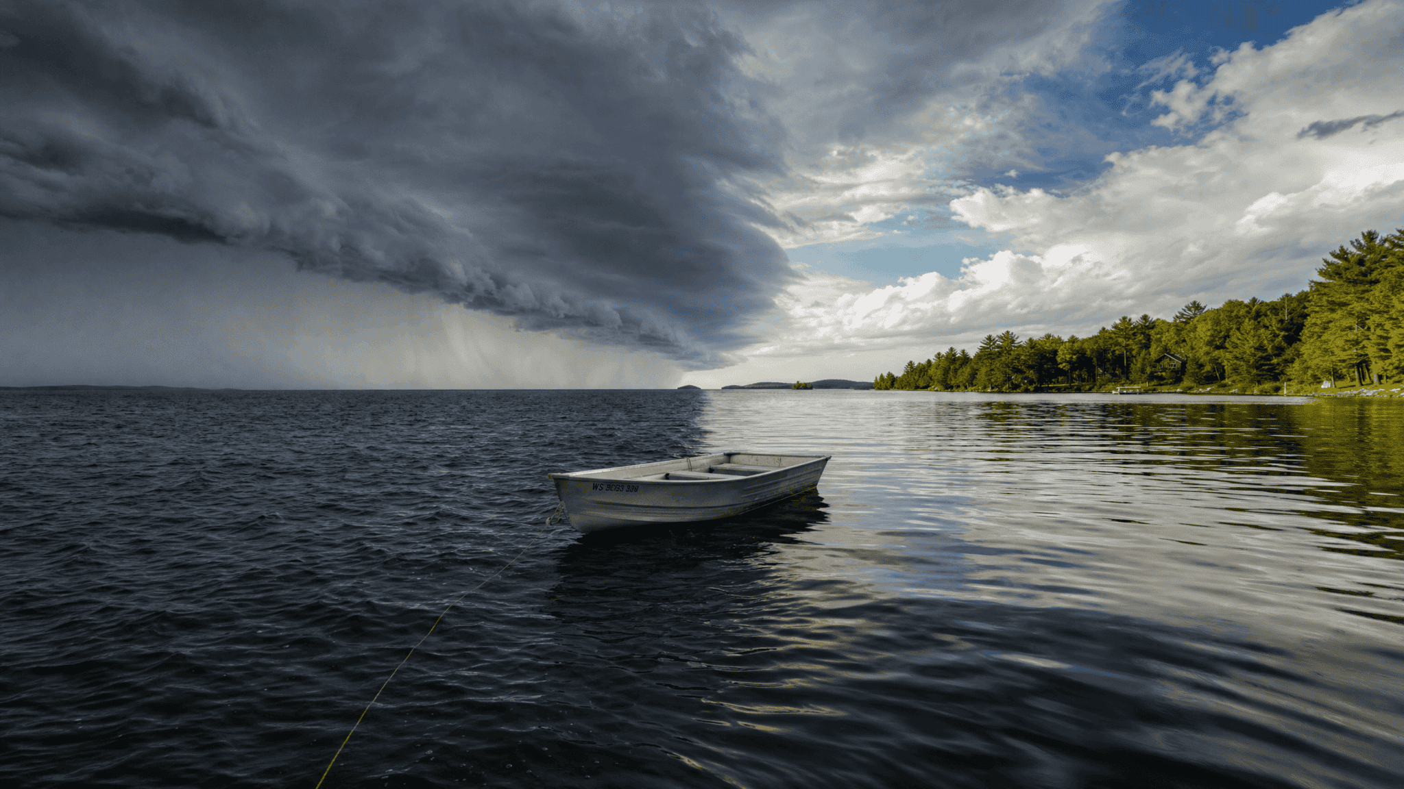 A weather front advancing across a lake with a dark cloud shelf and wind line, an anchored boat sitting on the dividing line