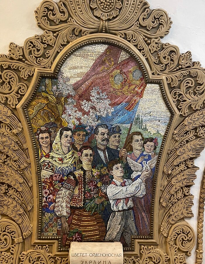 Decorative mosaic panel inside the Moscow metro showing figures, flags, and ornamental framing.